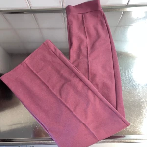 Rosa byxor från La Banga, USA - Snygga rosa kostymbyxor från La Banga med hög midja och dragkedja bak. Byxorna köptes från Miami i USA.  Byxorna har en elegant design med raka ben och är tillverkade i ett mjukt material som ger en bekväm passform.