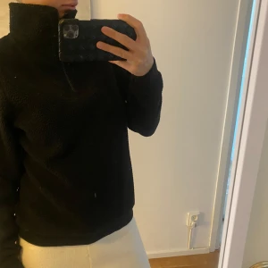 Svart fleece tröja med dragkedja - Mysig svart fleece tröja med hög krage och dragkedja. Perfekt för kyliga dagar och ger en avslappnad look. Tröjan har långa ärmar och en normal passform.