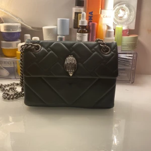 Kurt geiger väska mörkgrön🥰 - Snygg mörkgrön väska från Kurt Geiger med kedjerem och dekorativt spänne framtill. Väskan har en elegant design och är perfekt för att ge din outfit en stilfull touch. Den har en praktisk storlek för att bära dina nödvändigheter.Väskan är i nyskick och äkta!🥰❤️