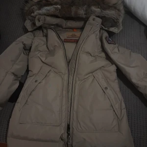 Beige dunjacka från Parajumpers - Säljer en snygg beige dunjacka från Parajumpers med pälsdetaljer på huvan. Jackan har en dragkedja framtill och praktiska fickor. Perfekt för kalla vinterdagar. 🧥❄️