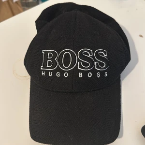 Svart keps från Hugo Boss - Snygg svart keps från Hugo Boss med broderad logotyp framtill. Perfekt för en stilren look. Justerbar passform för optimal komfort.