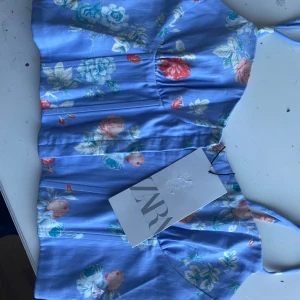 Blommig blå korsettopp från Zara - Säljer en söt blå korsettopp från Zara med blommigt mönster i olika färger. Toppen har smala axelband och en åtsittande passform. Perfekt för sommarens varma dagar! Prislapp kvar
