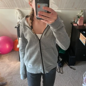 Grå hoodie från Andy by Frank Dandy - Säljer en grå hoodie från Andy by Frank Dandy. Den har en dragkedja framtill och en mysig fodrad insida. Perfekt för kyliga dagar. Hoodien har långa ärmar och en klassisk passform. Andvänd några gånger men i väldigt fint skick! Pris kan diskuteras!💕