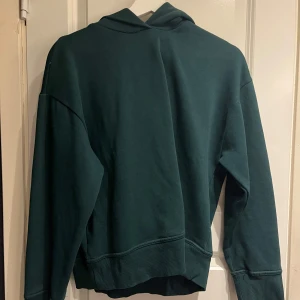 Mörkgrön hoodie från Zara - Säljer en stilren mörkgrön hoodie från Zara. Den har en klassisk design med huva och långa ärmar, perfekt för en avslappnad look. Materialet känns mjukt och bekvämt. Passar perfekt för kyligare dagar.