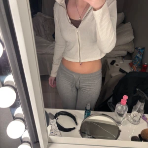 Vit ribbad kofta med dragkedja - Säljer en stilren vit ribbad kofta med dragkedja framtill. Koftan är croppad och har långa ärmar, perfekt för en trendig look. Passar bra till både jeans och kjol. Hör av dig vid intresse!