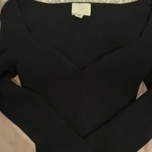 Svart ribbad tröja från H&M - Säljer en stilren svart ribbad tröja från H&M. Tröjan har en v-ringad design och långa ärmar, perfekt för en elegant look. Passar bra till både jeans och kjol. Perfekt för höst och vinter!