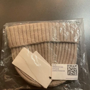 Beige ribbad mössa från H&M - Säljer en stilren beige ribbad mössa från H&M. Perfekt för att hålla värmen under kyliga dagar. Mössan är en del av deras baby exclusive kollektion och kommer i en neutral färg som passar till det mesta. Ull. 