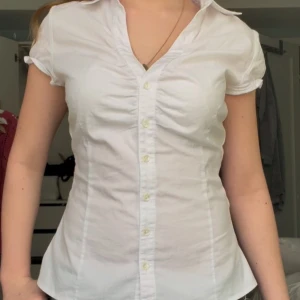 Vit kortärmad blus - Säljer en stilren vit blus från Plick  med korta ärmar och knappar framtill. Perfekt för en chic och enkel look. Passformen är normal och materialet är bomull, vilket gör den bekväm och lätt att bära. Har även sytt in den själv!