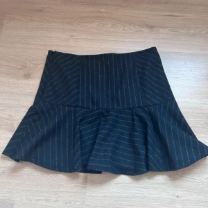 Svart kjol med volang från Lindex - Snygg svart kjol från Zara med subtila ränder och volangdetalj. Perfekt för en stilren look. Kjolen har en normal passform och är tillverkad i ett bekvämt material.