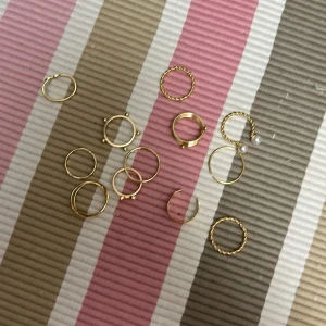 Guldiga ringar med pärldetaljer - Ett set av 12 guldiga ringar i olika stilar, inklusive tvinnade och släta designer. Vissa ringar har pärldetaljer och en har en stjärnformad design. Perfekt för att mixa och matcha för en personlig stil.