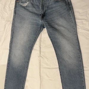 Blå jeans från Levi's - Snygga ljusblå jeans från Levi's med klassisk femficksdesign och en liten slitning på bakfickan. Perfekta för en avslappnad stil. De har en rak passform och är tillverkade i slitstarkt denim.