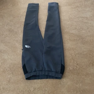 Grå mjukisbyxor från The North Face - Säljer ett par grå mjukisbyxor från The North Face. Byxorna har en bekväm passform med elastisk midja och ribbade muddar vid bensluten. Perfekta för en avslappnad stil.
