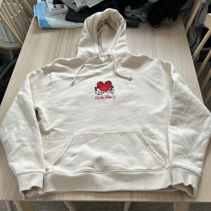 Beige hoodie från Axel Arigato - Säljer en snygg beige hoodie från Axel Arigato med en röd hjärtapplikation och texten 'Kiss Han' på framsidan. Tröjan har en klassisk känguruficka 