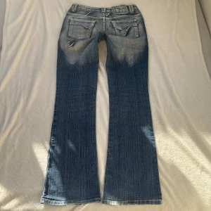 As coola jeans med slitningar - Snygga blå bootcut jeans med coola slitningar och broderade detaljer. Midjemåttet tvärs över är 38cm och innerbensländen är 83cm🤍