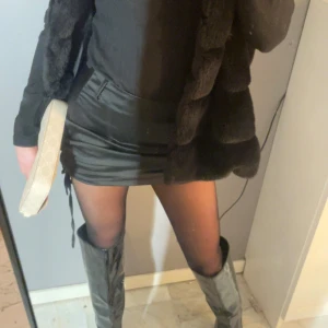 Svart kortkjol i skinnimitation - Trendig svart kortkjol i skinnimitation med en tight passform. Kjolen har en stilren design och passar perfekt för en kväll ute. Den är enkel att matcha med olika toppar och accessoarer.