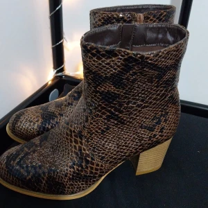 Bruna boots med ormmönster - Snygga bruna boots med ormmönster och dragkedja på sidan. Skorna har en robust klack och är perfekta för att ge din outfit en edgy touch. Perfekta för höst och vår.