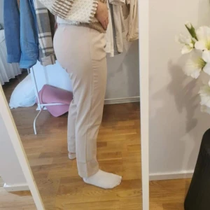 Beige kostymbyxor - Snygga beige kostymbyxor med hög midja och rak passform. Byxorna har en klassisk design med knappar och dragkedja framtill. Perfekta för en stilren look.