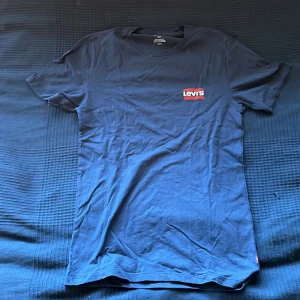 T-shirt från Levi's i blått och vitt - Två snygga t-shirts från Levi's, en i marinblå och en i vit. Båda har det klassiska Levi's-logotypen tryckt på bröstet. Perfekta för en avslappnad stil.