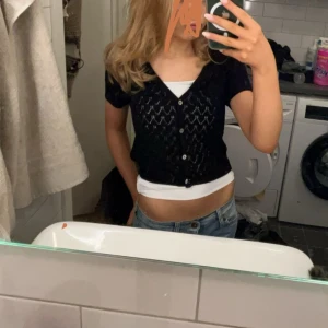 Svart kortärmad kofta - Säljer en svart kortärmad kofta med knappar framtill. Koftan har ett diskret mönster och är perfekt för lager-på-lager-stil. Passar bra till jeans eller kjol.