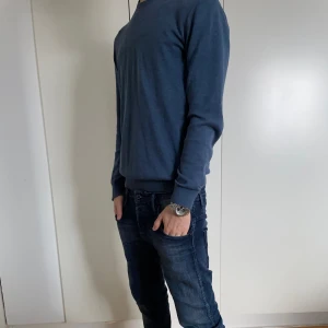 Blå långärmad tröja från Bläck - Säljer en stilren blå långärmad tröja med rund hals. Perfekt för en avslappnad look. Tröjan har en normal passform och är tillverkad i ett mjukt material. Skick 7/10 finns ett litet hål i armhålan kom provat för bild. Modellen är 173