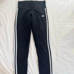 Low waist leggings från Adidas - Snygga svarta leggings från Adidas med vita ränder längs sidorna. Perfekta för träning eller en avslappnad dag. 