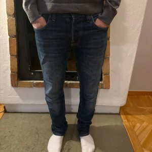 Mörkblå jeans från Nudie Jeans - Snygga mörkblå jeans från Nudie Jeans med klassisk femficksdesign och orange sömmar. De har en straight passform och är perfekta för en avslappnad stil. Midjan är midwaist och de har en knappgylf.