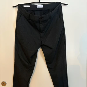 Svarta kostymbyxor  - Eleganta svarta kostymbyxor med en stilren design. Byxorna har en knapp- och dragkedjestängning och är perfekta för en sofistikerad look. Storlek 32/34