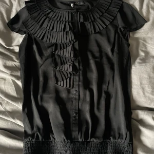 Svart topp - Svart topp med volanger. Lappen fortfarande kvar. Säljer då den inte kommer till användning.