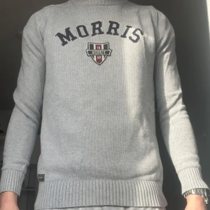 Grå tröja från Morris Gents - Snygg grå tröja från Morris Gents med broderad logga på bröstet. Tröjan har långa ärmar och ribbade muddar vid ärmslut och nederkant. Perfekt för en stilren look. Skriver storlek M för jag är 185 och väger 70 och den passar M