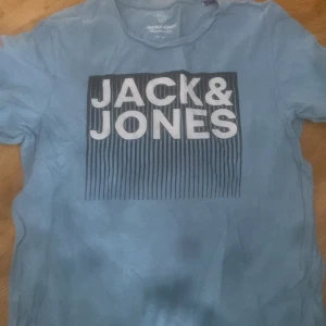 Blå t-shirt från Jack & Jones - Säljer en blå t-shirt från Jack & Jones med ett stort tryck på framsidan. T-shirten har korta ärmar och är perfekt för en avslappnad stil. Den är gjord i ett mjukt material som känns skönt mot huden.