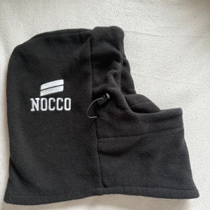 Svart fleecehuva från NOCCO - Säljer en svart fleecehuva från NOCCO. Den är perfekt för kalla dagar och har en justerbar dragsko för bättre passform. Huvan är mjuk och bekväm. 