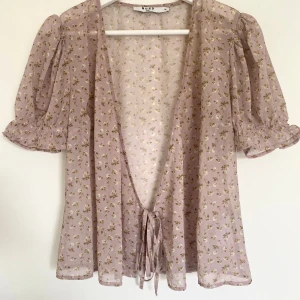 Blommig blus från NA-KD!🫶🏻🎀 - Superfin blommig omlottblus från NA-KD i storlek 36. Den är i en ljuslila nyans med små blommor på. Blusen har korta puffärmar och en knytning framtill!🎀🫶🏻🌷