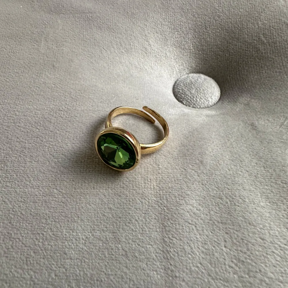 Säljer en snygg guldfärgad ring från Pilgrim med en stor, glittrande grön sten!  Guldpläterad ring med grön kristall. En symbol för hopp till din smyckessamling Justerbar storlek med kristall på 15 mm i diameter 100 % glam piece Tillverkat av 80% återvunnet material. Nypris: 399kr. Accessoarer.