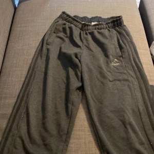 Svarta mjukisbyxor från Adidas - Säljer ett par svarta mjukisbyxor från Adidas. De har en bekväm elastisk midja och är perfekta för en avslappnad stil. Byxorna har Adidas-loggan på sidan och är gjorda i mjukt material för extra komfort.