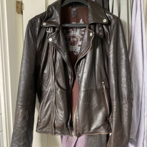 Brun Läderjacka från Gipsy - Säljer en snygg brun skinnjacka från Gipsy. Den har en cool bikerstil med dragkedja och knappar framtill. Jackan är långärmad och har en klassisk krage. Perfekt för höst och vår!   Den är i bra skick men är väl använd vilket har gjort den mjukare och smidigare. Den har två relativt rymliga fickor på insidan förutom de som syns på bilderna där en kan stängas med dragkedja och en med knapp, men där knappen tyvär försvunnit. Det är storlek medium med den är lite större och lösare i min åsikt. 😊