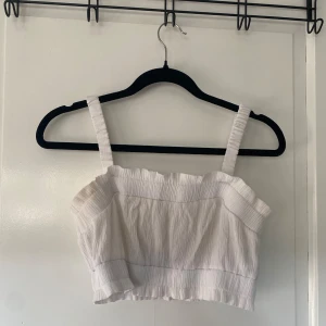 Vit ribbad topp - Säljer en superfin vit ribbad topp med breda axelband. Den är perfekt för sommardagar och har en bekväm passform. Toppen är i ett stretchigt material som gör den både snygg och skön att bära. Passar perfekt till både jeans och kjol!