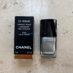 Chanel Le Vernis Longwear Nail Colour 540 Liquid Mirror - Säljer ett superlyxigt nagellack från Chanel i färgen 540 Liquid Mirror. Det är en långvarig nagelfärg som ger en spegelblank finish. Flaskan innehåller 13 ml och kommer i en elegant svart förpackning med guldiga detaljer. Perfekt för en glamorös look!