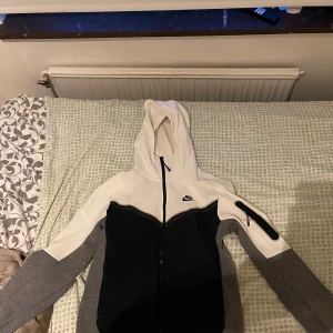 Nike huvtröja i grått och vitt - Säljer en snygg, sällsynt och bekväm Nike huvtröja i svart, grått och vitt. Den har en dragkedja framtill och en praktisk ficka på ärmen. Perfekt för både träning och vardag. Storlek S.