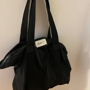 Svart axelväska från Day Birger et Mikkelsen - Säljer min fina svarta axelväska från Day Birger et Mikkelsen. Väskan är i syntetmaterial och har en praktisk dragkedja upptill. Perfekt som skolväska eller när du behöver ha med dig lite extra grejer. Den är stor och i bra skick💕