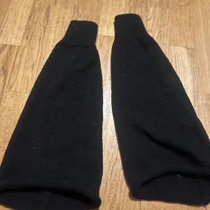 Svarta benvärmare  - Svarta benvärmare i enkel design, perfekta för kyligare väder. De är långa och ser ut att vara gjorda av ett mjukt material som ger bra värme.