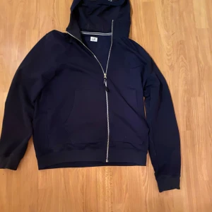 Mörkblå huvtröja från C.P. Company - Säljer en mörkblå huvtröja från C.P. Company med dragkedja och unika glasögondetaljer på huvan. Perfekt för en stilren och avslappnad look. Tröjan har långa ärmar och en praktisk ficka framtill. Ny skick skriv om ni är intresserade 