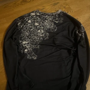 Svart långärmad tröja med skelettmönster - Cool svart tröja med lång ärm och detaljerat skelettmönster i vitt. Perfekt för en edgy stil.