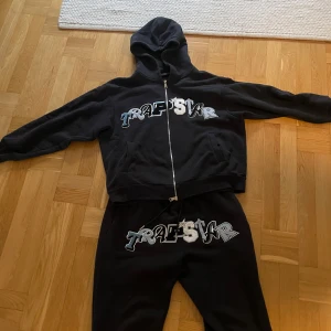 Svart hoodie från Trapstar - Säljer en svart hoodie från Trapstar med dragkedja och tryck på bröstet. Perfekt för en avslappnad stil. Hoodien har långa ärmar och en bekväm passform. Resselar för ungefär 220£ sälja nu till ett väldigt bra pris 