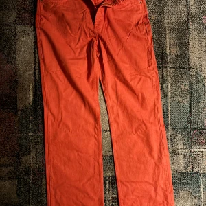 Orange byxor - Snygga orange byxor med en rak passform. Perfekta för att lägga till en färgklick i garderoben. Byxorna har en klassisk design med fickor och knappstängning.