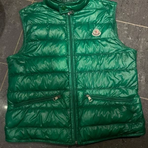 Grön dunväst från Moncler - Snygg grön dunväst från Moncler med dragkedja och broderad logga på bröstet. Perfekt för kyligare dagar och ger en stilren look. Västen har praktiska fickor med dragkedja. Västen är i väldigt fint skick, motsvarande 9/10 ✅. Storlek 2. Hör av er vid frågor, kan tänka mig byten ❗️ 