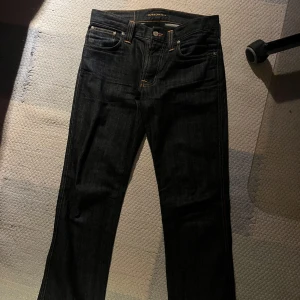 Svarta jeans Nudie Jeans Slim Jim Dry Broken Twill - Säljer ett par svarta/mörk blå jeans från Nudie Jeans, modell Slim Jim. De är tillverkade i 100% bomull och har en slim passform. Säljer dem för att de inte passar mig längre, jättefint skick. Storlek 30/32. Nypris ligger på 1200kr