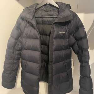 Svart Peak Performance dunjacka - Svart dunjacka från Peak Performance med anpassningsbar huva och midja. Jackan är i 80% ankdun och 20% fjäder och perfekt för vinter och kalla dagar. Nypris är ca 4000kr.