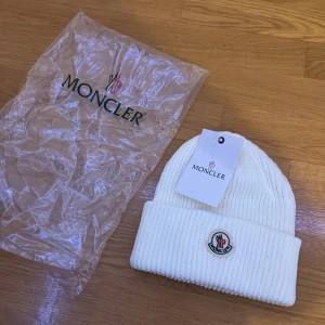 Cream vit ribbad mössa från Moncler - Snygg vit ribbad mössa från Moncler med broderad logotyp framtill. Perfekt för att hålla värmen under kyliga dagar. Stilren design som passar till det mesta. OBS! Kontakta mig för att köpa dessa, eller köp från dom andra anonserna i min profil!