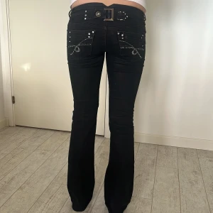Svarta lågmidjade bootcut jeans med detaljer - Snygga svarta bootcut jeans med låg midja och glittriga detaljer på bakfickorna. Byxorna har stretch, midjemått 36 och innerbenslängd 82. Det saknas något diamant men inget som man lägger märke till