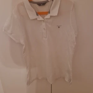 Vit kortärmad polotopp från Gant - Säljer en klassisk vit polotopp från Gant med korta ärmar och knappdetaljer framtill. Perfekt för en stilren och avslappnad look.